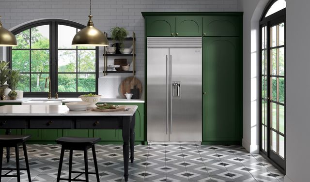front view of a contemporary kitchen with a white, green, and gold color palette, and a sub-zero stainless steel refrigerator built into the green cabinetry